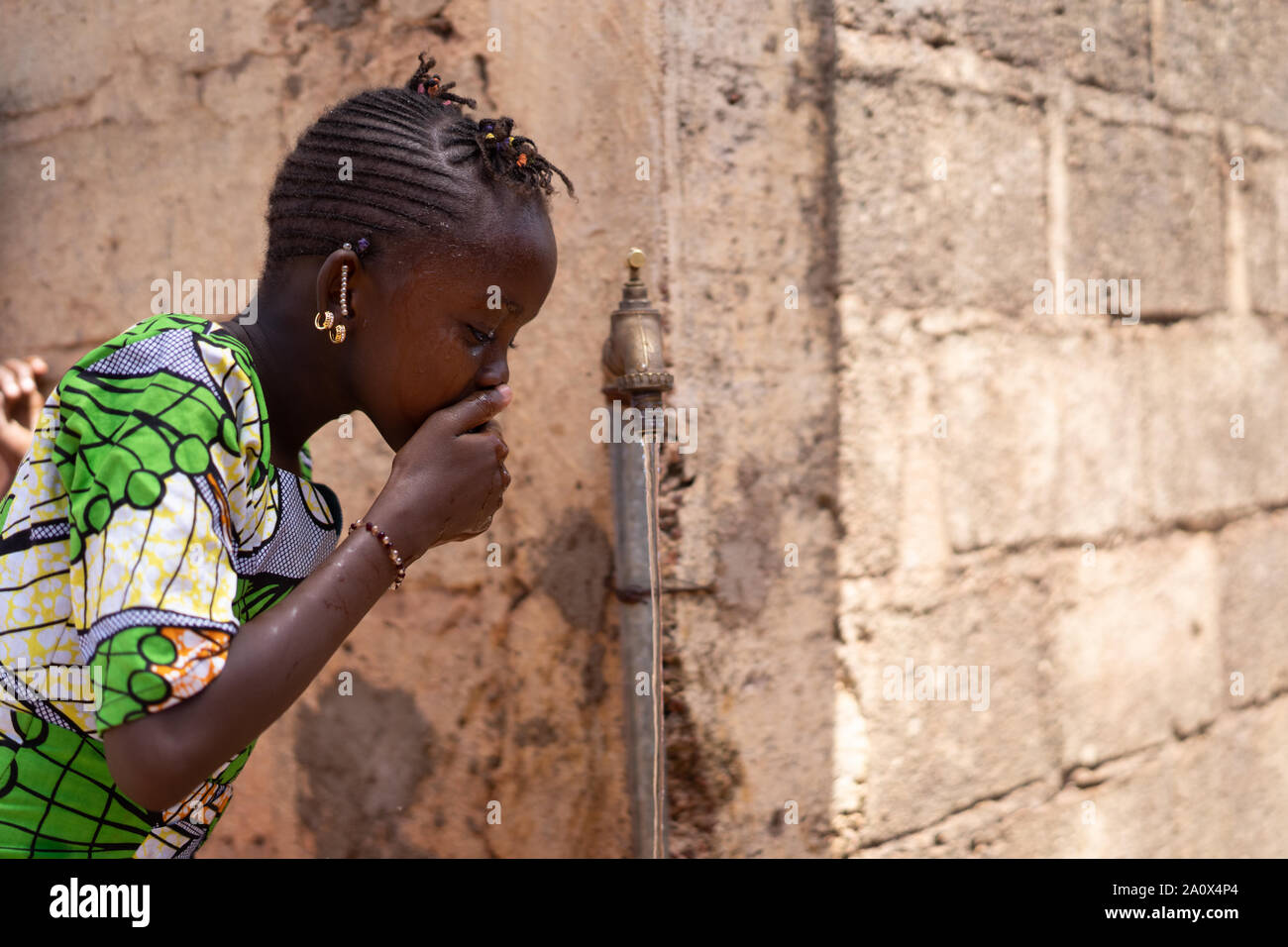 Preschooler bevande di acqua dolce pulita da un rubinetto di Bamako, in Mali Foto Stock