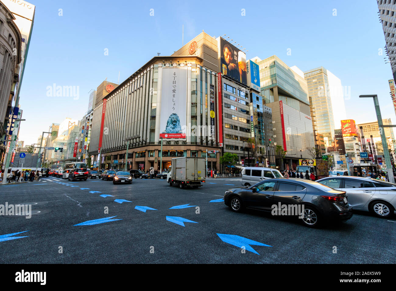 Tokyo, il Ginza 4 interscambio con traffico verso il passato e flagship Mitsukoshi department store di fronte. Ora d'oro, nel tardo pomeriggio. Blue sky. Foto Stock