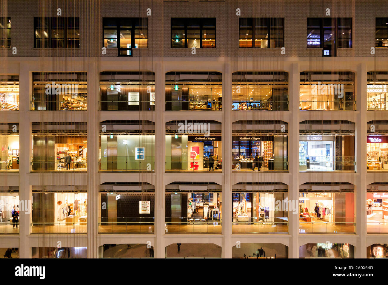 Tokyo, Marunouchi. KITTE building interior. Tre piani di quattro negozi aperti ciascuno su un lato del triangolo atrium. Onitsuka Tiger store. Notte. Foto Stock
