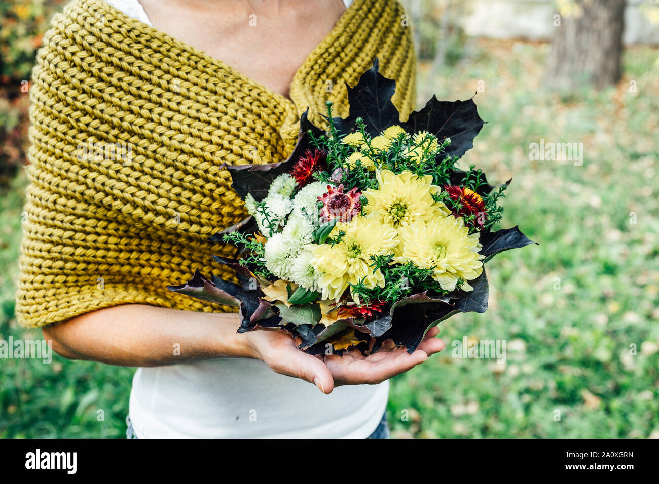 Donna elegante in una maglia di cachi snood detiene un autunno bouquet di fiori e foglie di acero Foto Stock
