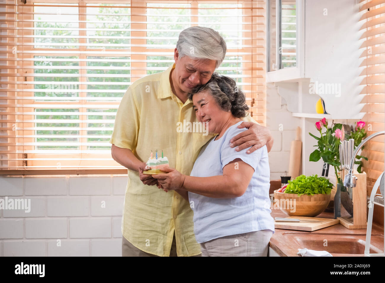 Asian senior sorpresa uomo donna senior con torta di compleanno in cucina a casa.abbracciando e godendo di trascorrere del tempo togethe, invecchiamento a home concetto Foto Stock