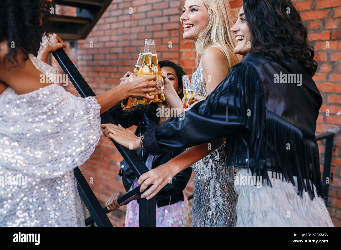 Il gruppo di donne aventi le bevande insieme. Amici di sesso femminile la tostatura con bottiglie di birra mentre passeggiate in città. Foto Stock