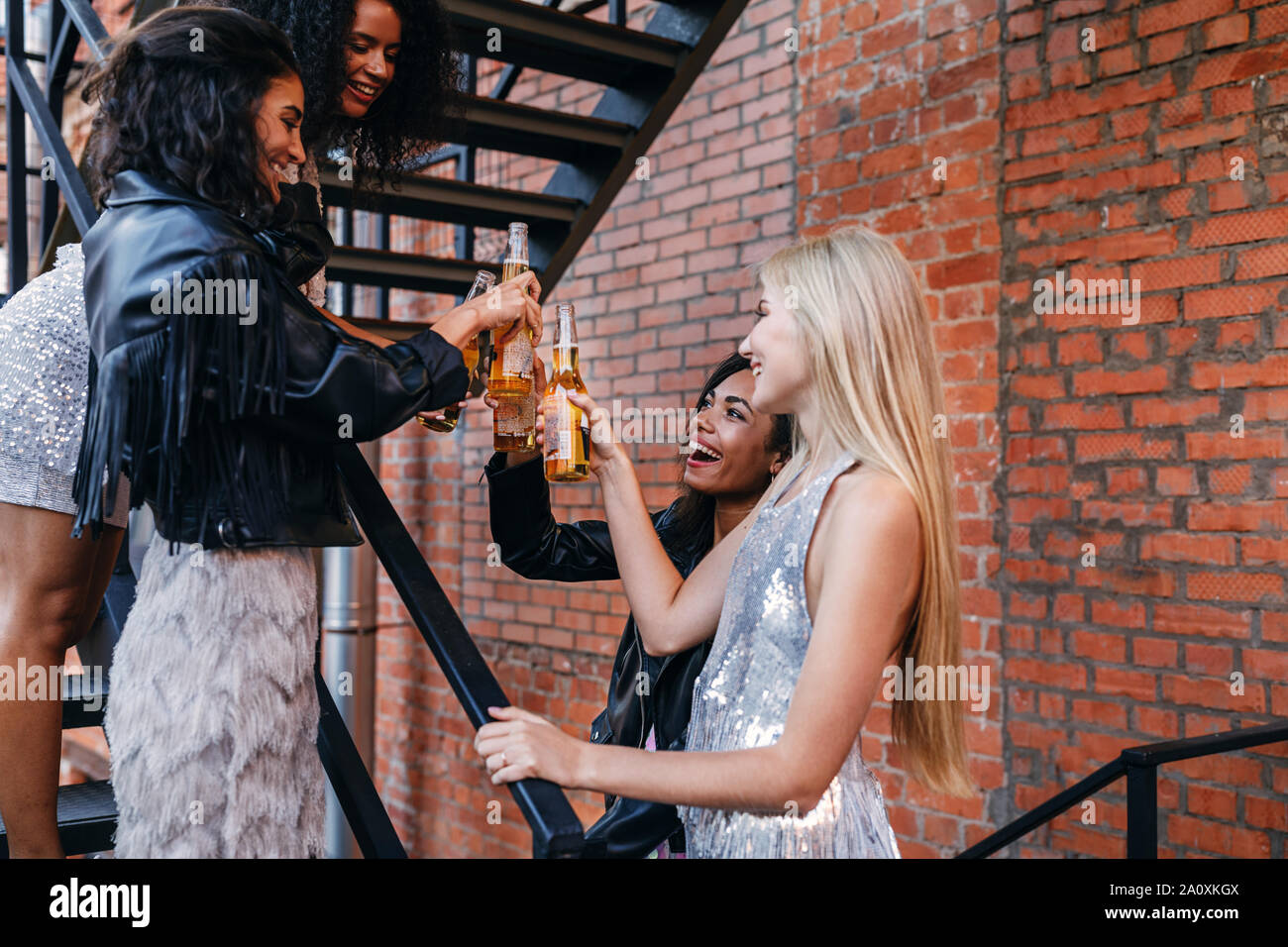 Gli amici di tostatura di bottiglie di birra su scala. Elegante donne celebrando all aperto con bicchieri di bevande alcoliche. Foto Stock