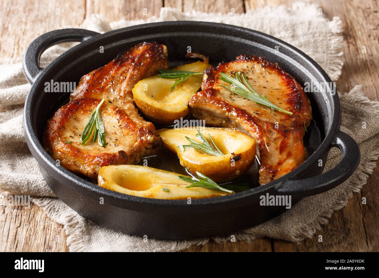 Piccanti cotte costolette di maiale con pere e rosmarino in miele-salsa di aglio servita in una padella vicino sul tavolo orizzontale. Foto Stock
