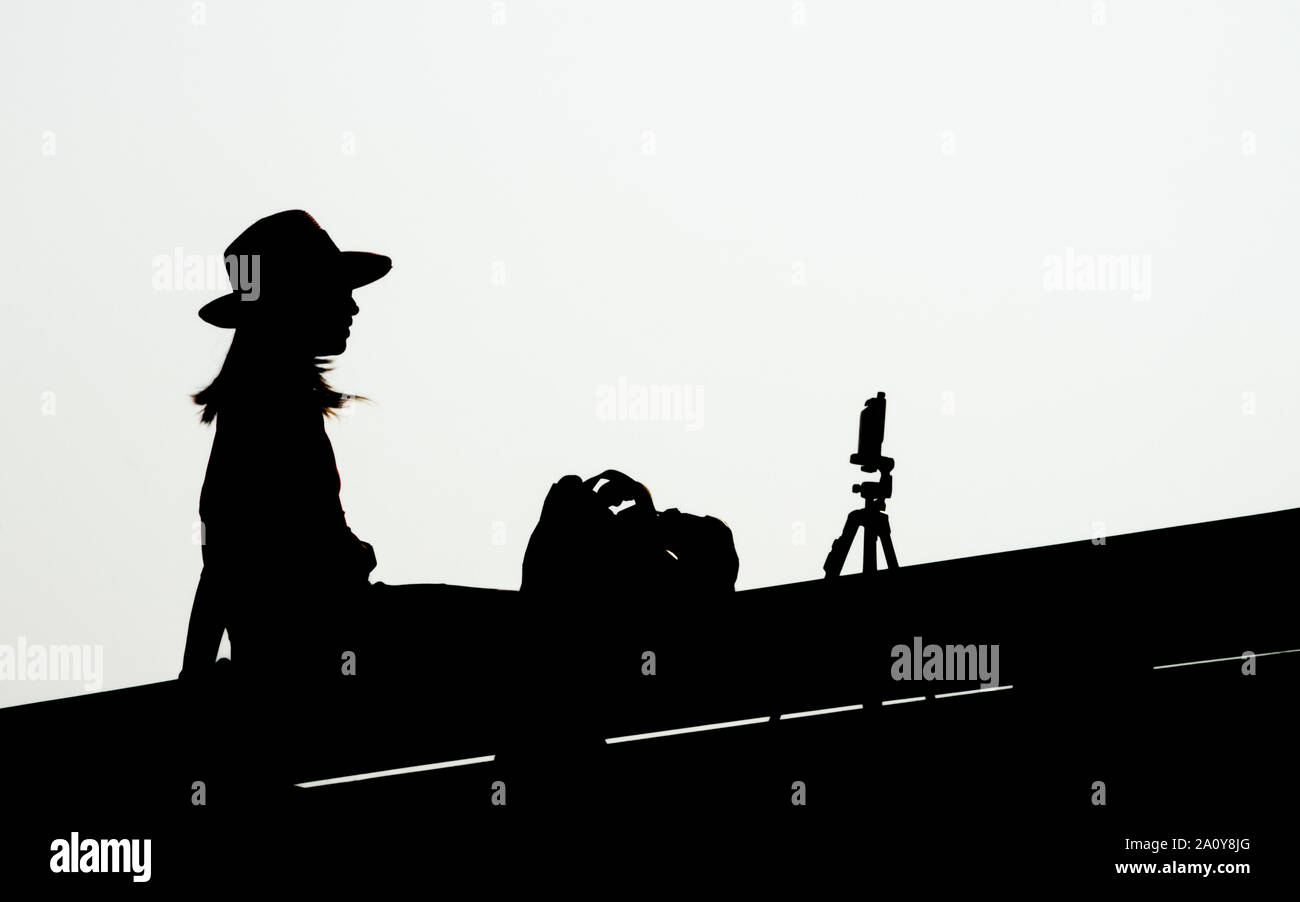 Silhouette di donna giovane con lo smartphone sul cavalletto tenendo selfies su sfondo bianco Foto Stock