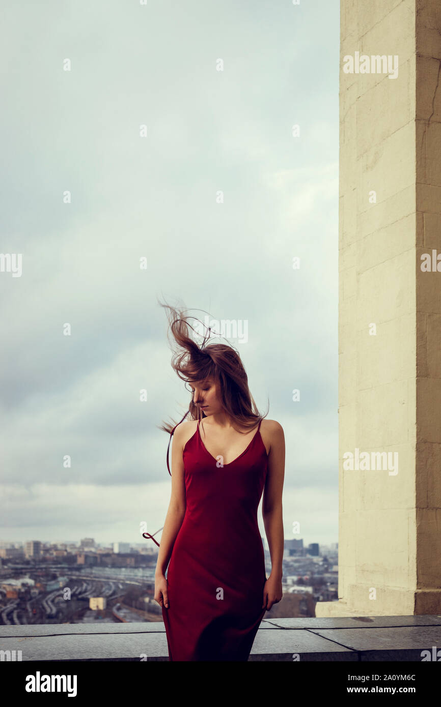 Slim ragazza in abito rosso è in piedi sulla sommità del grattacielo, alta sopra la megacity,diffusione dietro di lei fino all'orizzonte.I suoi capelli al vento Foto Stock