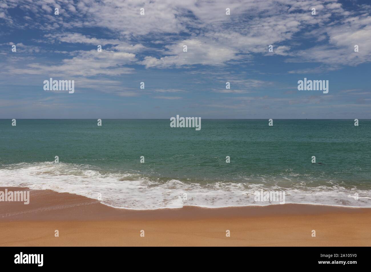 Il pittoresco paesaggio marino con acque azzurre, cielo blu e nuvole bianche. Vista la schiuma delle onde oceaniche lappatura presso la riva sabbiosa Foto Stock