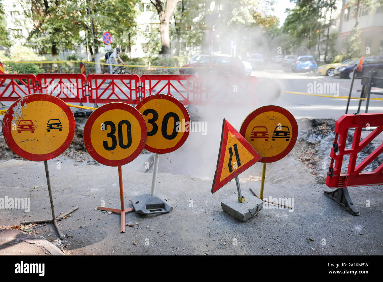 Il traffico stradale cartelli di avvertimento e un recinto di plastica intorno ad un grande buco nell'asfalto da dove esce vapore Foto Stock