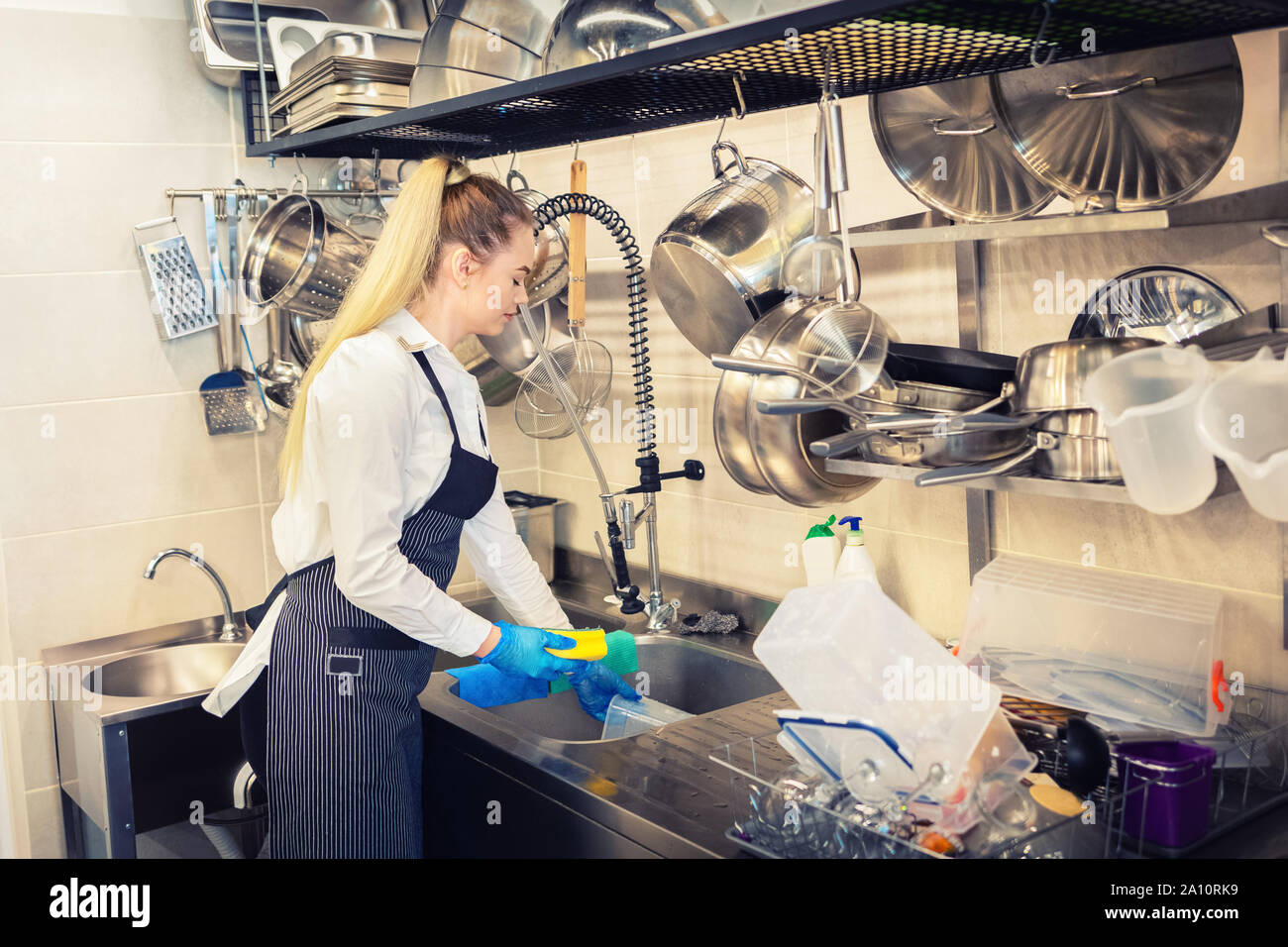 Cameriera di lavaggio piatti nel lavandino alla fine della giornata di lavoro in cucina professionale Foto Stock