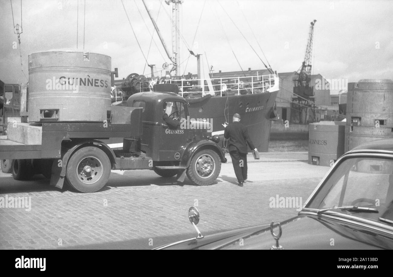 Spedizione di birra Guinness in metallo gigante di birra in fusti (serbatoi trasportabili) dal carrello al dock per essere caricati su navi da carrelli elevatori a forche, Dublino, Eire c. 1955 Foto Stock