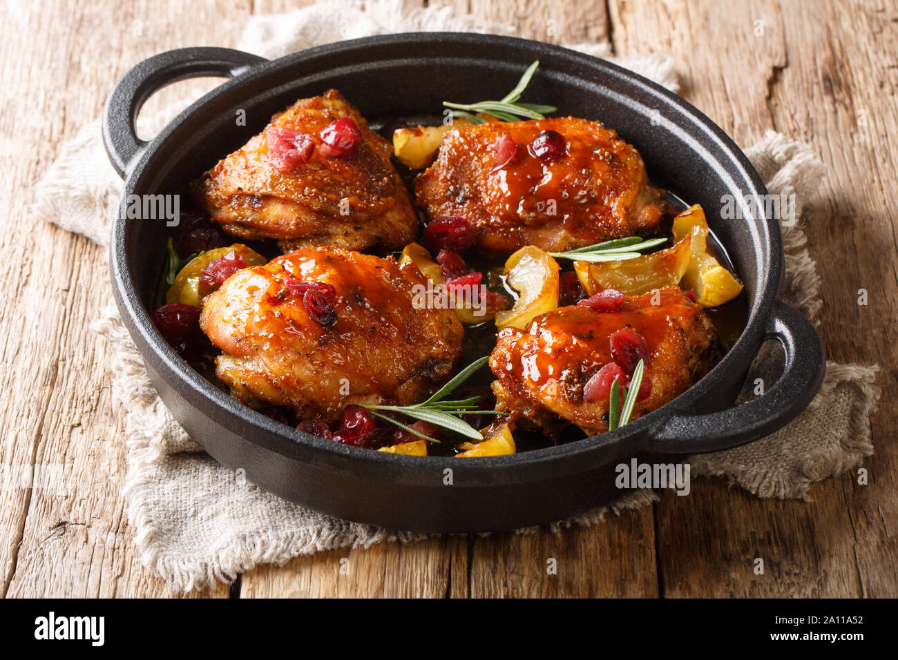 Holiday caldi i cibi cotti al forno cosce di pollo con mele, mirtilli e rosmarino closeup in una padella sul tavolo orizzontale. Foto Stock