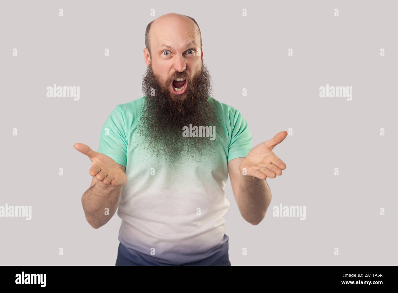 Cosa vuoi fare? Ritratto di angry medio di età compresa tra uomo calvo con barba lunga in verde chiaro t-shirt in piedi, guardando la telecamera, urlando e chiedendo ind. Foto Stock