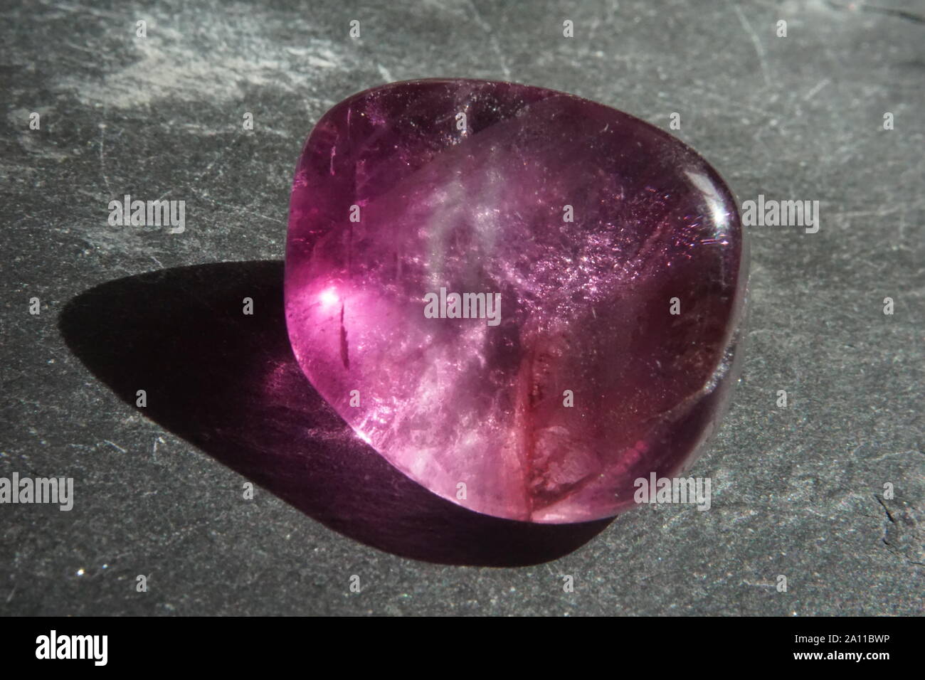 Le riprese in modalità macro di fluorite viola burattati ciottolo su grigio ardesia sfondo Foto Stock