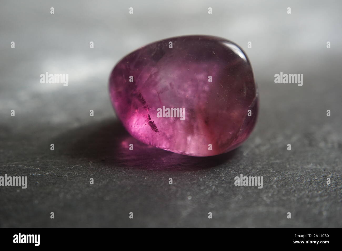 Le riprese in modalità macro di fluorite viola burattati ciottolo su grigio ardesia sfondo Foto Stock