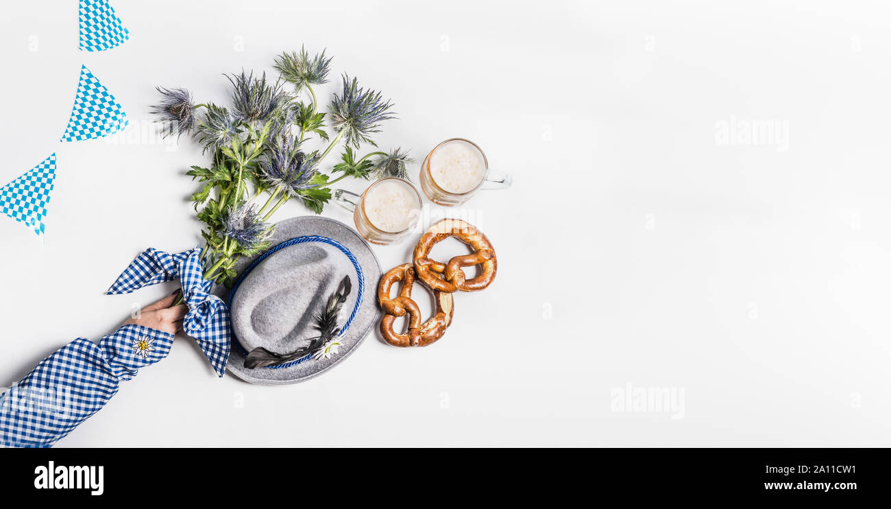 Oktoberfest sfondo . Boccali di Birra bavarese, con cappello di piume pretzel, donna mano nella tradizionale blu camicetta e fiori alpini. Vista dall'alto. Moderno. Foto Stock