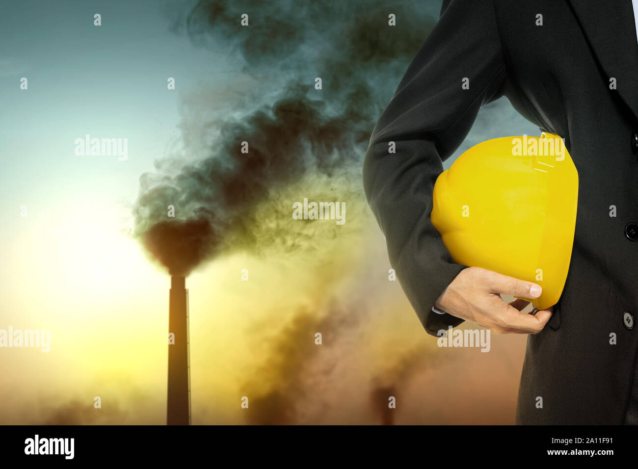 La gente di affari con un cappello giallo sulla sua mano con camino e inquinamento atmosferico dall'attività industriale nella città Foto Stock