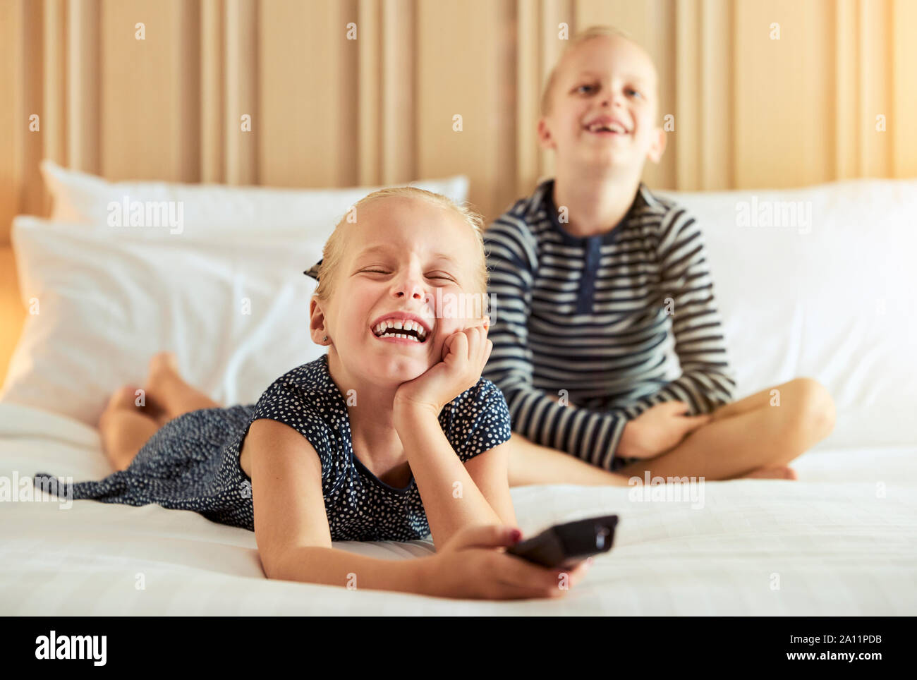 Ridere bambina e suo fratello carino guardando la televisione togeter mentre vi rilassate in un letto Foto Stock
