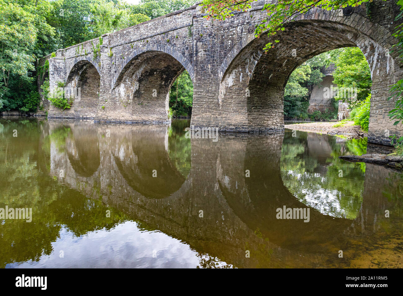 Estate dettagliata vista guardando fino al fiume Torridge, attraverso lo storico ponte Rothern al ponte di Rolle con acqua bassa e di riflessioni: Torrington. Foto Stock