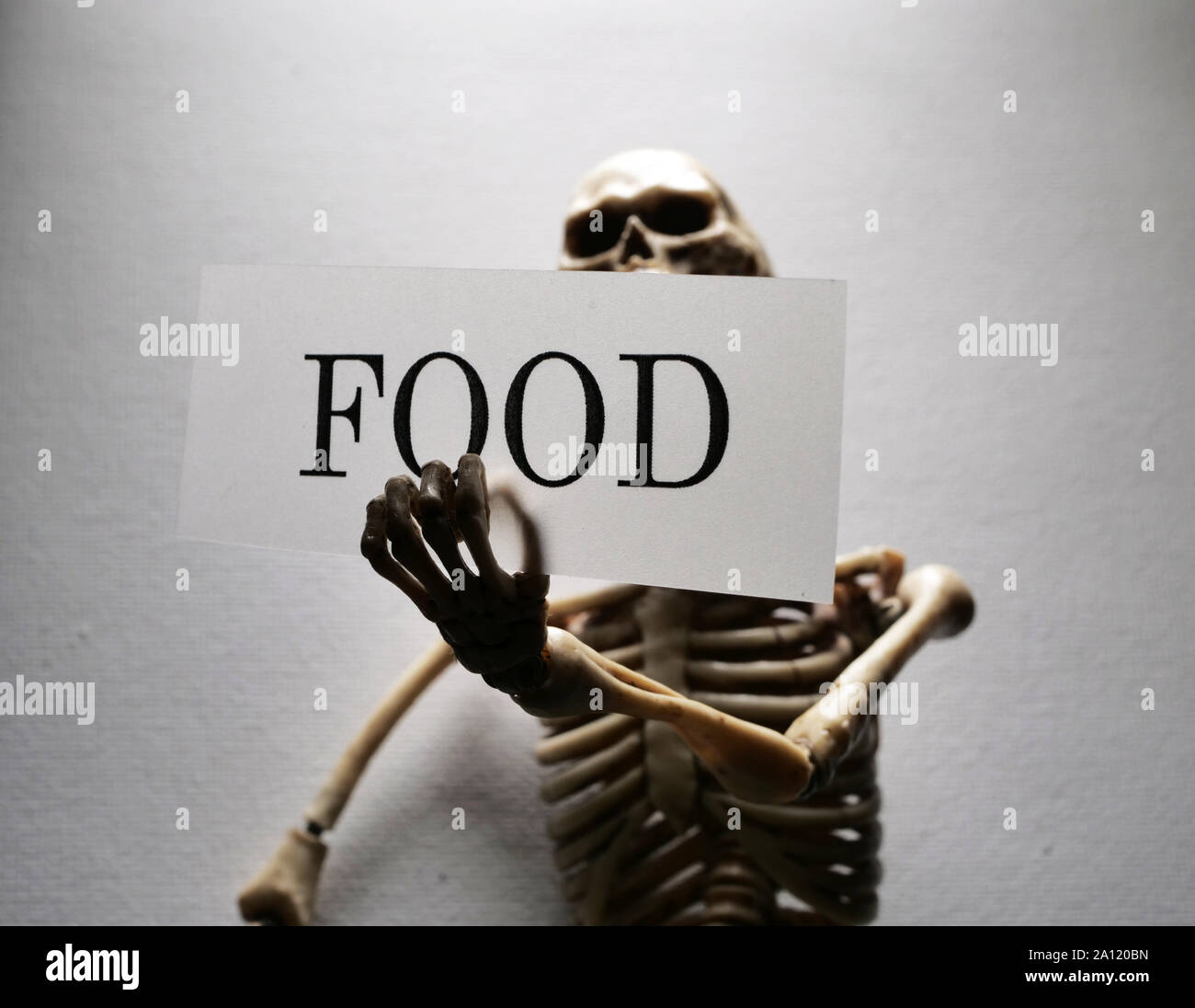 Lo scheletro tenendo un cibo etichetta della tag che implica la mancanza di cibo Foto Stock