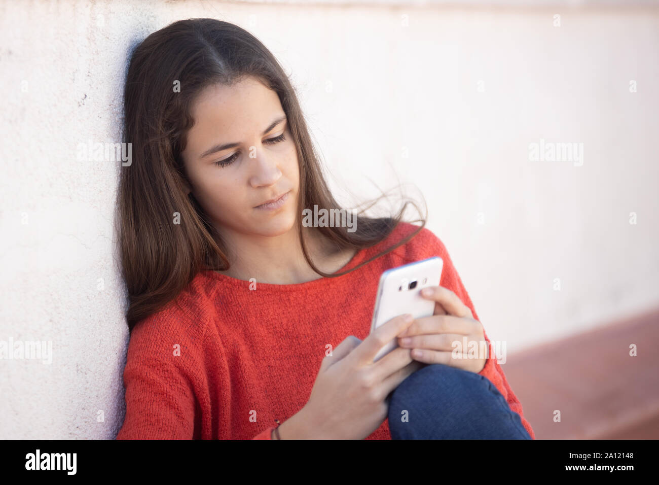 Chica adolescente feliz mirando el smartphone sentada en la azotea Foto Stock