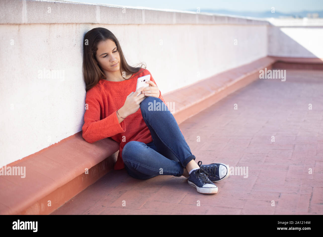 Chica adolescente mirando el smartphone sentada en la azotea Foto Stock