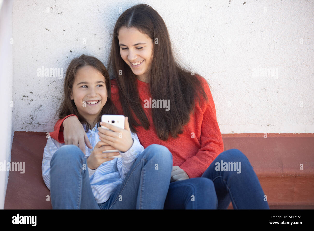 Dos Hermanas mirando el smarthphone sentadas en la azotea Foto Stock