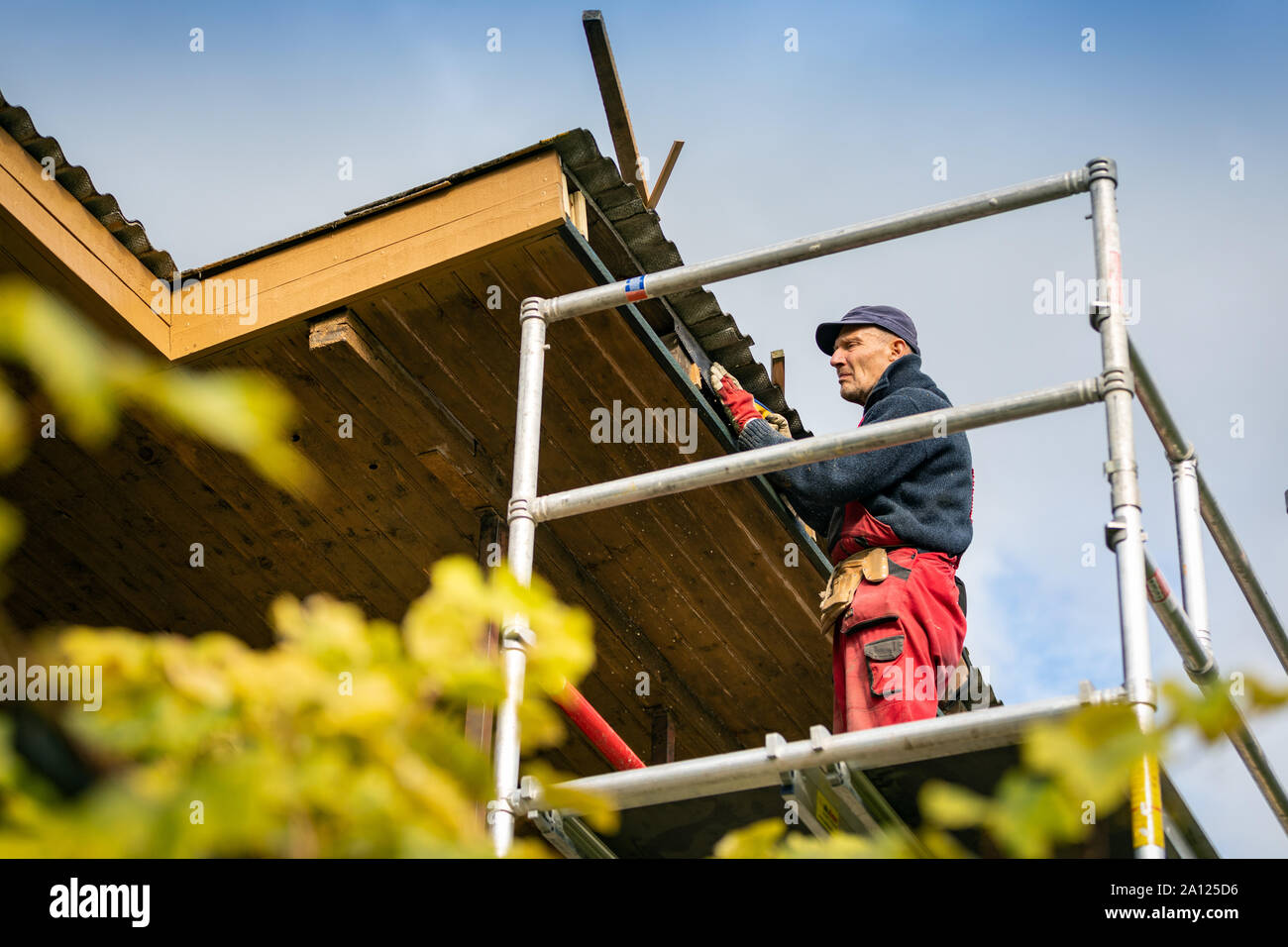 Lavoratore su impalcature in legno rinnovando la struttura del tetto Foto Stock