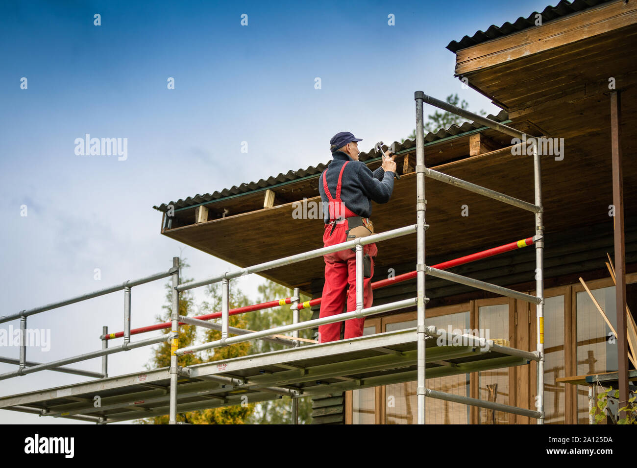 Uomo in piedi su un ponteggio e ripristinare la vecchia casa in legno della struttura del tetto Foto Stock