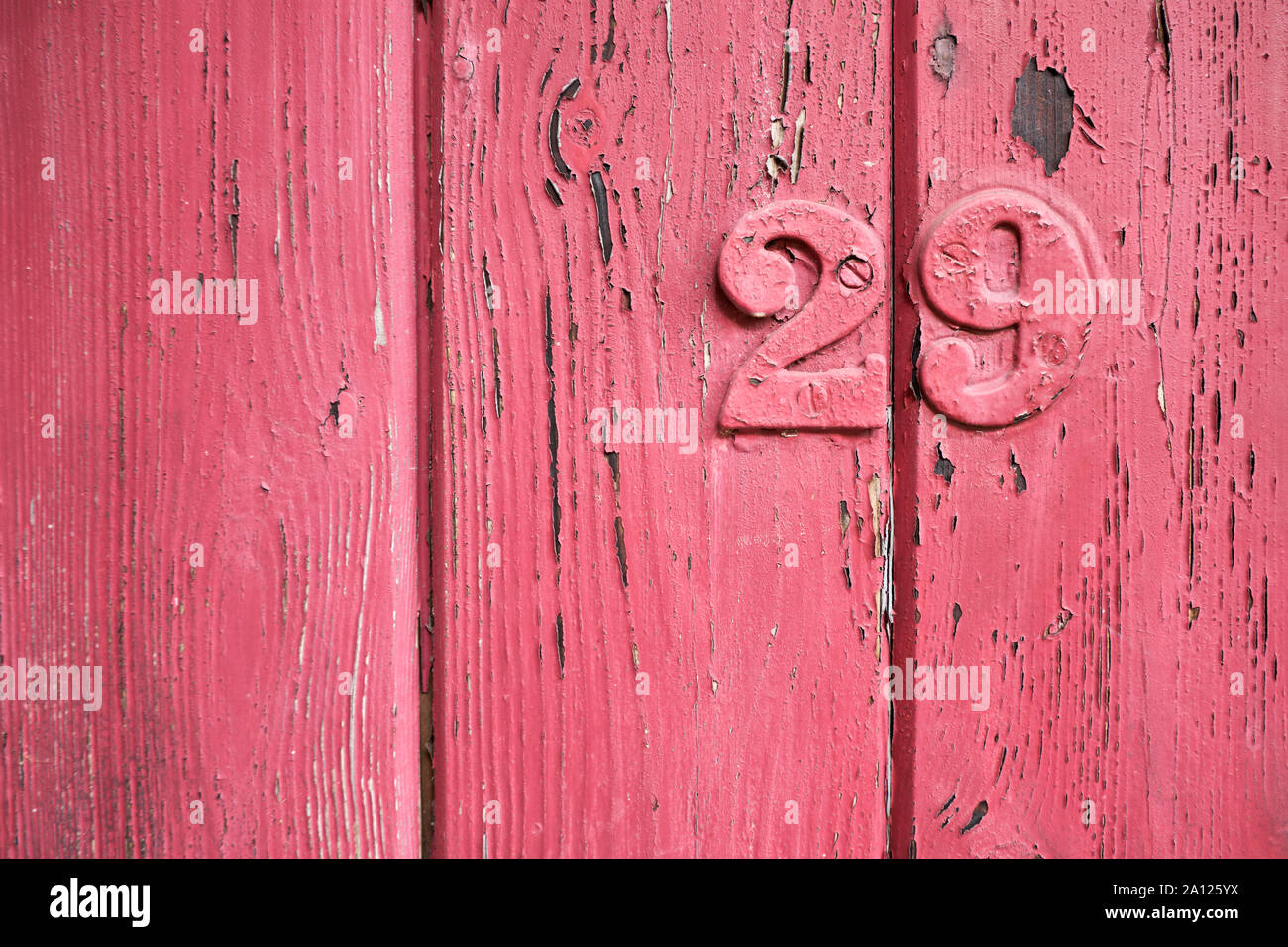 Rustico invecchiato closeup del pannello in legno dipinto di rosso con colore di scheggiatura. Verticale con doghe legno verticale texture di linee e il numero di metallo 29 sopra dipinta Foto Stock