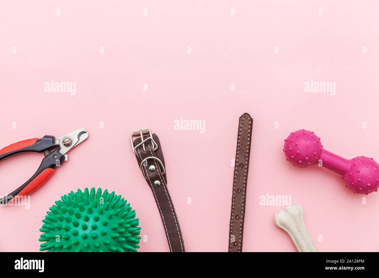 Pet care e concetto di animali. Giocattoli e accessori per cane per la riproduzione e la formazione isolato sul rosa pastello sfondo alla moda. Lay piatto con sfera osso clicker taglierina ad artiglio collare. Vista dall'alto uno spazio di copia Foto Stock