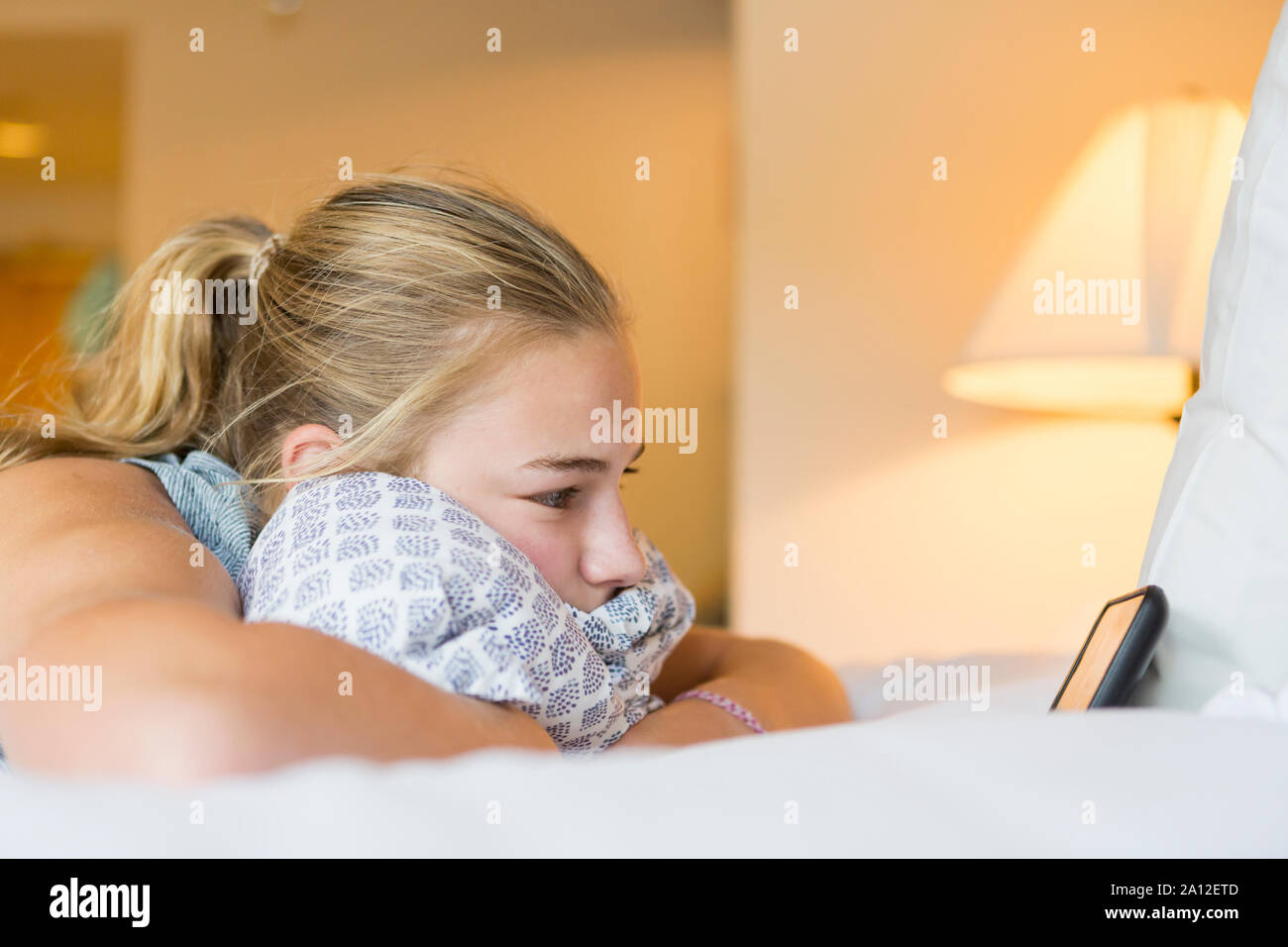 13 enne ragazza distesa sulla camera di albergo bed guardando smart phone Foto Stock