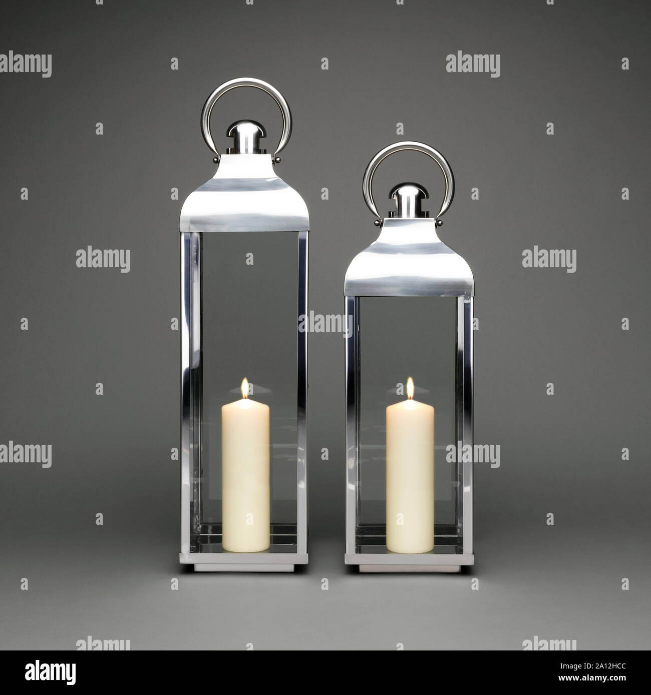 Due grandi candela lanterne di contenimento, con candele accese su uno sfondo grigio scuro. Foto Stock