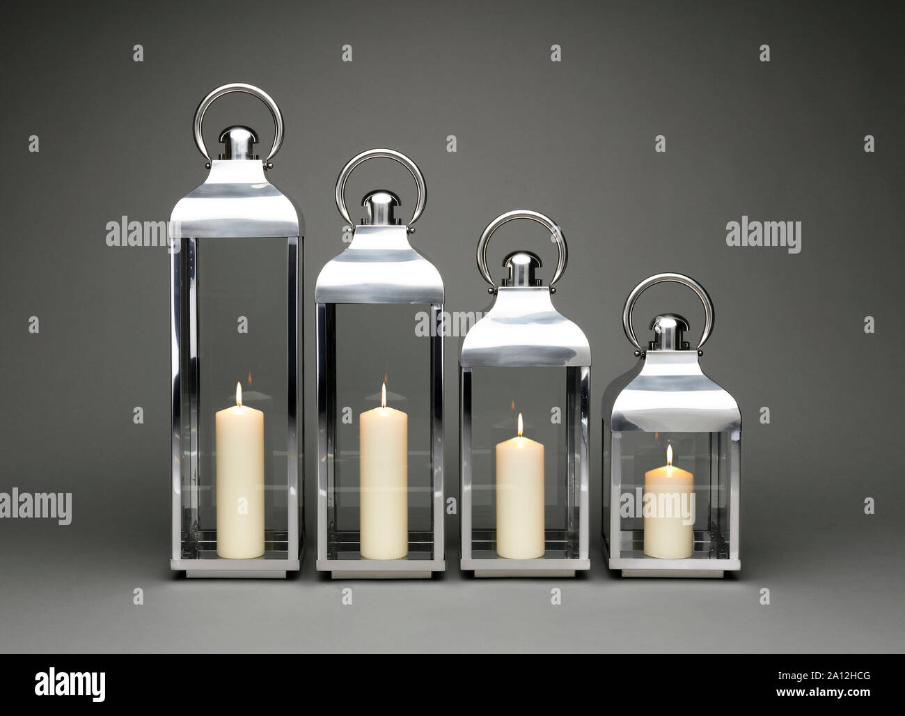 Una linea di quattro candele lanterne di contenimento, con candele accese su uno sfondo grigio scuro. Foto Stock