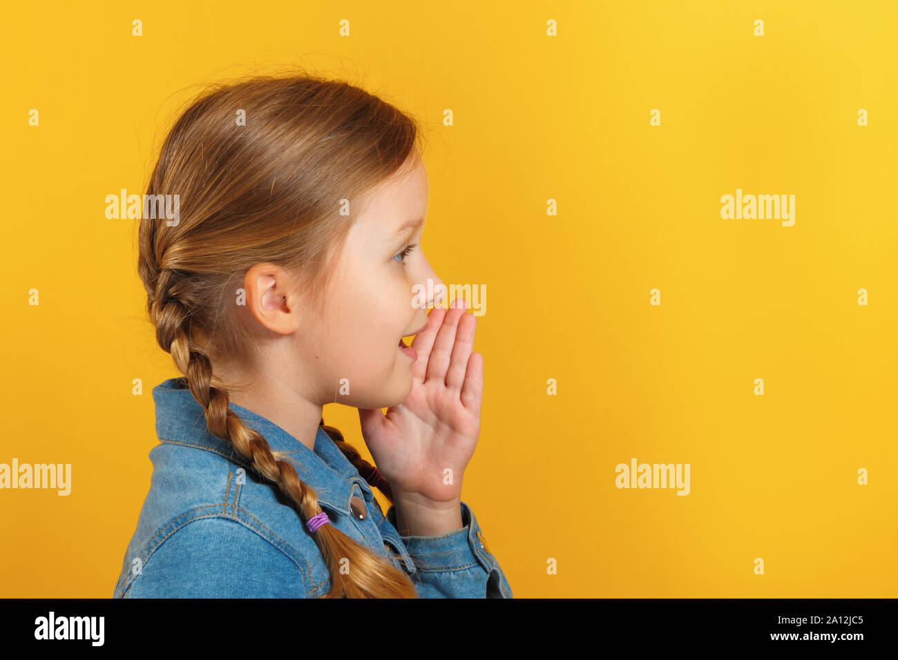 Profilo del bambino in vista laterale. La bambina parla in disparte, tiene una mano in corrispondenza di una bocca. Foto Stock