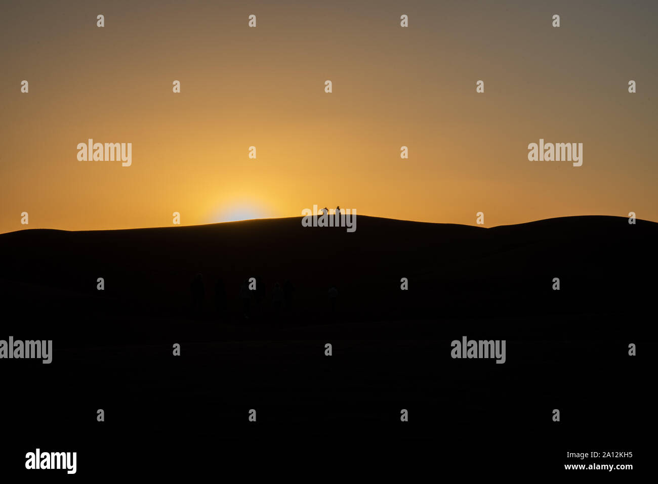 Gruppo di turisti a guardare il tramonto nel deserto su una collina a Mhamid, Maroc Foto Stock