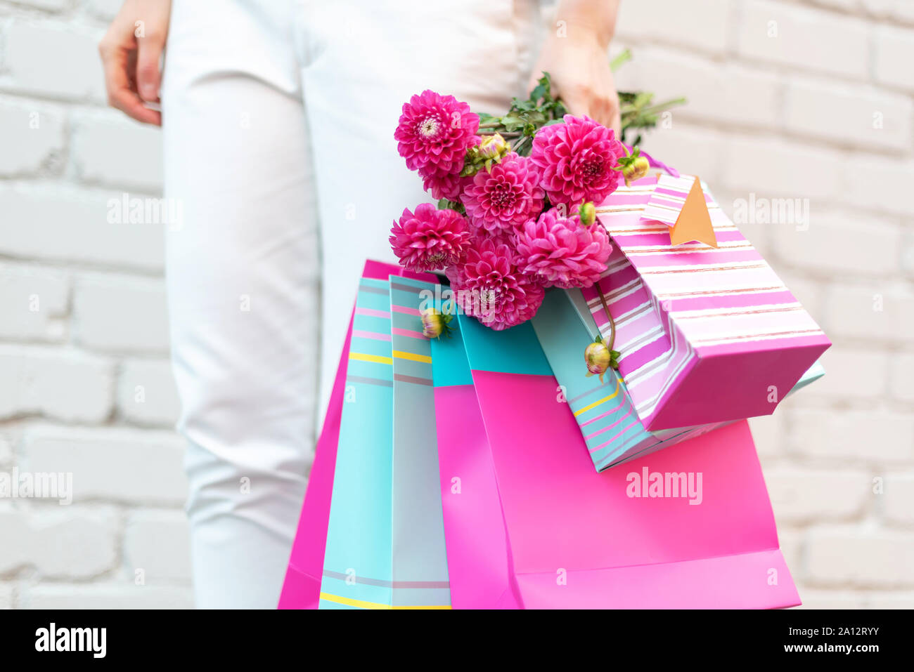 Fiori di colore rosa nel femminile la mano e borse per lo shopping su sfondo mattone. Compleanno, madre, Donna giorno di nozze concetto. Mazzetto di carta buste regalo. Foto Stock