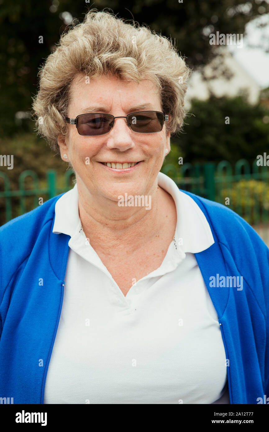 Un ritratto di un senior donna sorridente in un bowling green. Indossa gli occhiali da sole. Foto Stock