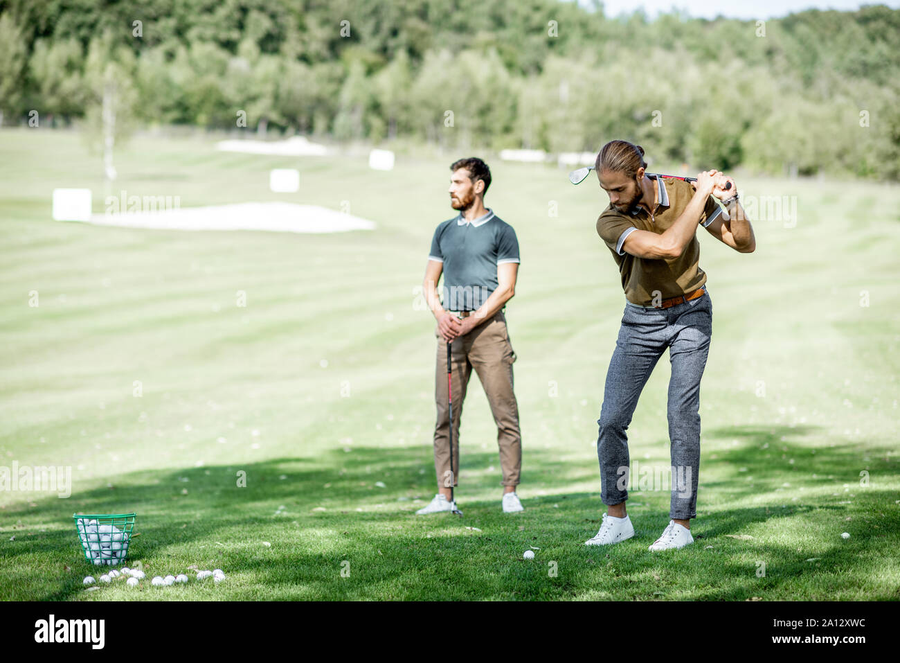 Due maschi amici per giocare a golf sul campo da golf, uomo oscillazione un putter Foto Stock