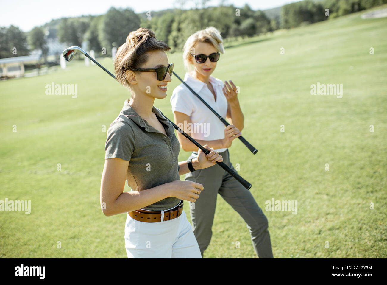 Due femmina migliori amici camminare insieme con la riproduzione di putters durante una partita di golf su un corso in una giornata di sole Foto Stock