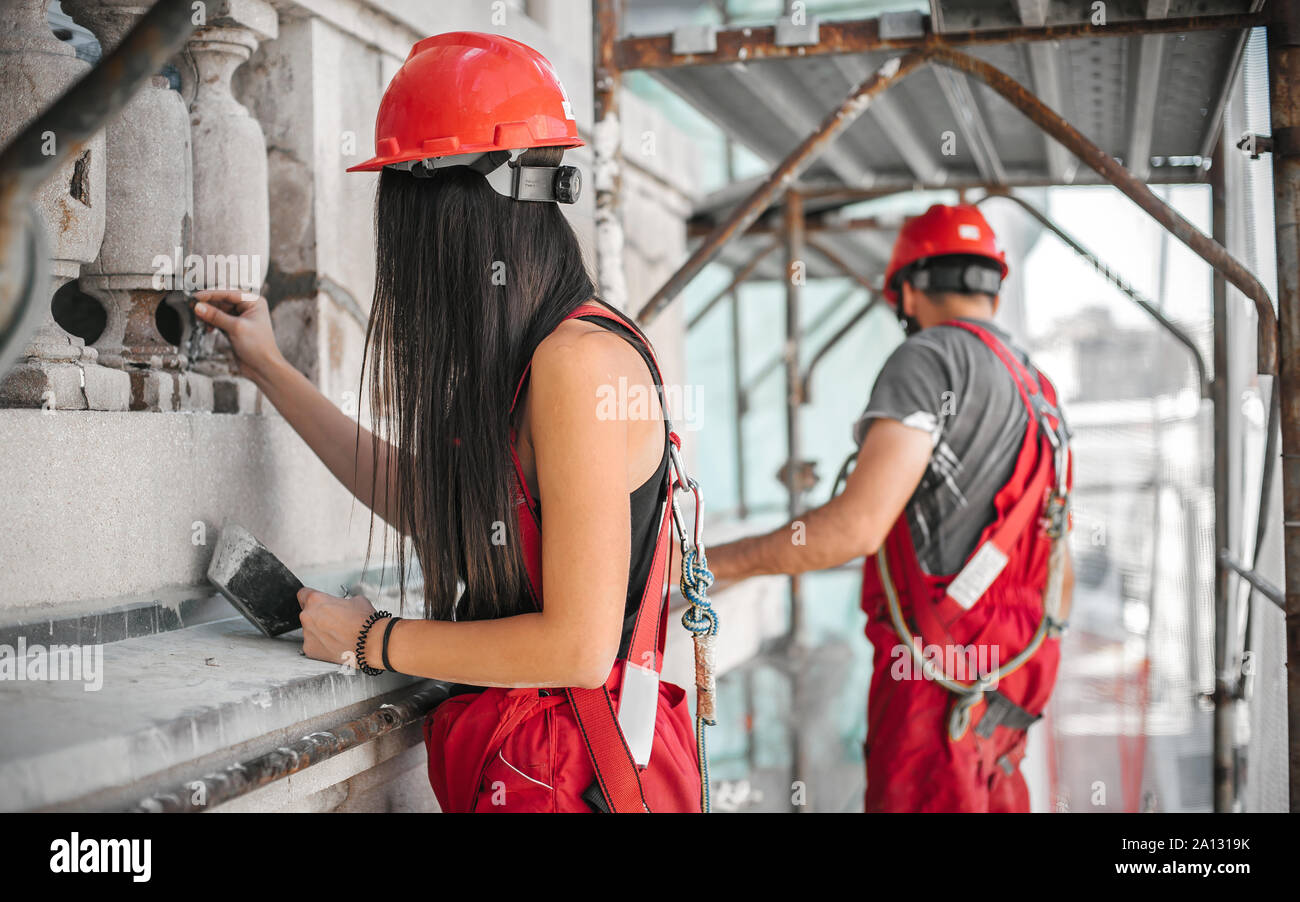 Due lavoratori in piedi su un ponteggio, eseguire lavori sul restauro della facciata del vecchio edificio. Riparazione e rinnovo Foto Stock