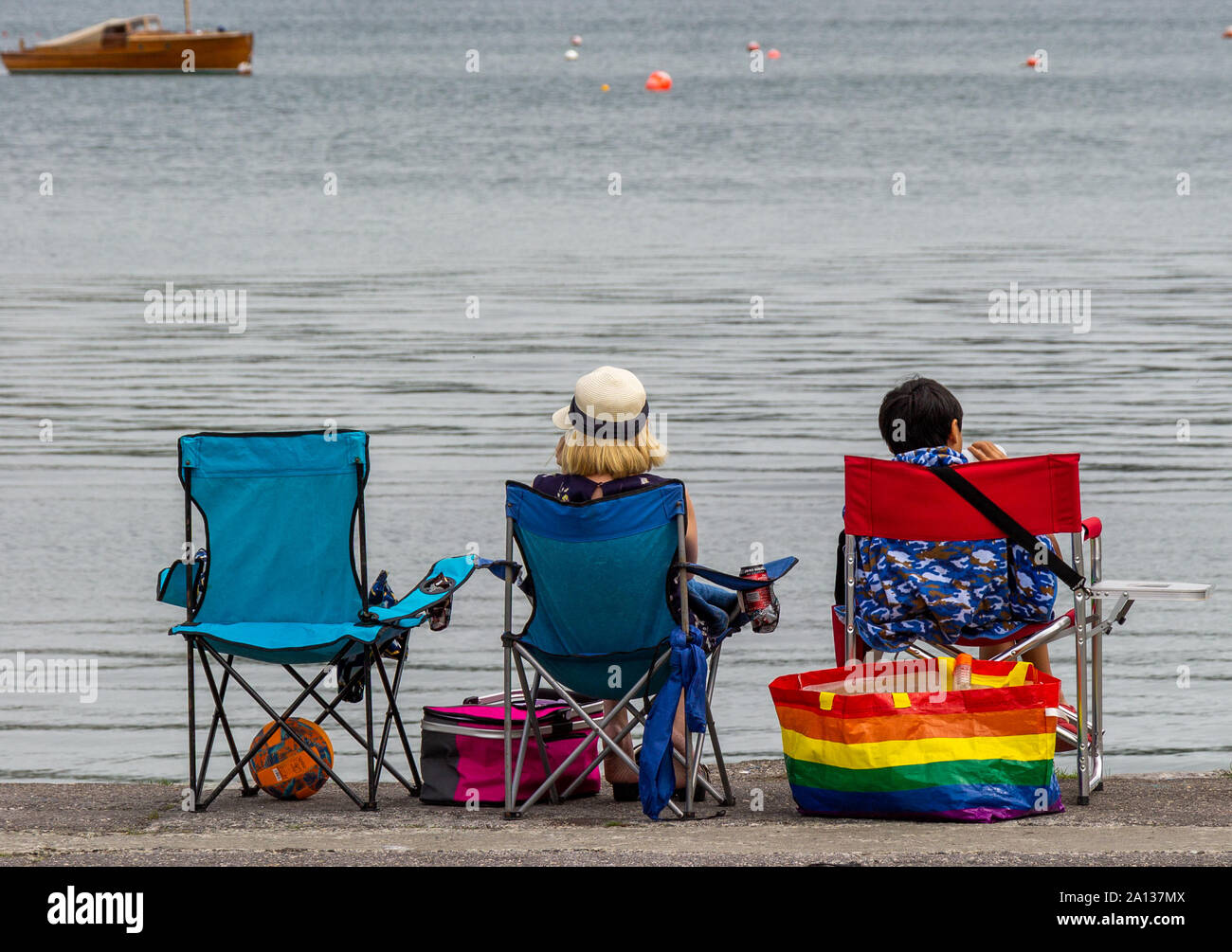 Le persone in vacanza si pose a sedere presso il mare di sedie che guarda al mare Foto Stock