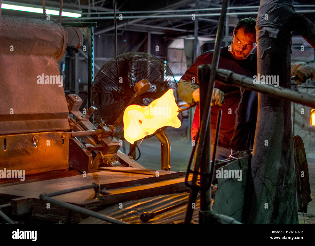 27 sett 2019 Kokomo Indiana America;un lavoratore di vetro utilizza strumenti di ferro e guanti pesanti per il sollevamento p un mucchio di vetro fuso. Egli ha poi impasti e volute i colori Foto Stock