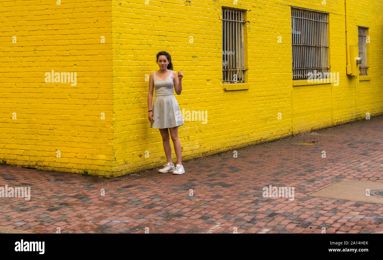 Teen in piedi accanto al giallo brillante con parete cellulare in mano Foto Stock
