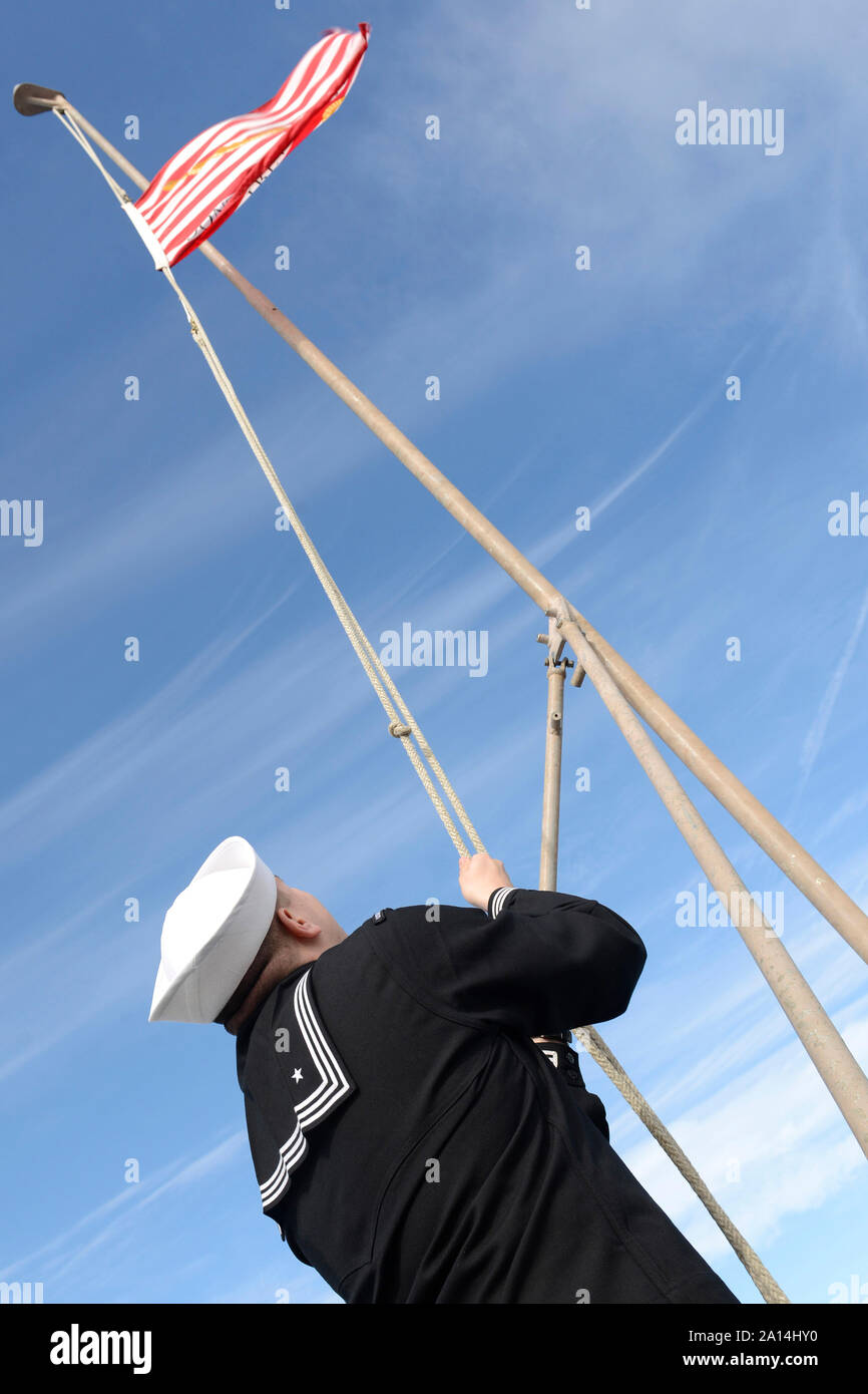Tecnico elettronico abbassa la Union Jack sul ponte di volo della USS Iwo Jima. Foto Stock