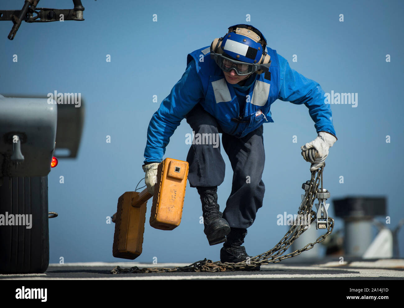 Boatswainâ€™s Mate marinaio rimuove tacchi e catene da un elicottero. Foto Stock