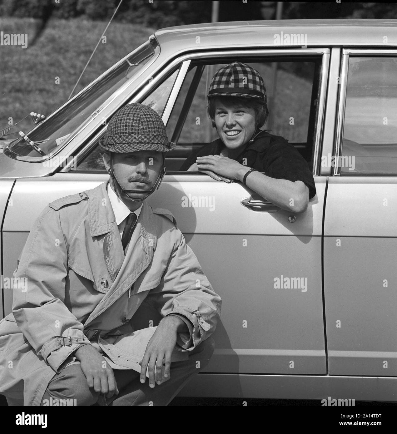 La guida negli anni sessanta. Caschi per auto è stato introdotto in Svezia a encrease sicurezza personale durante la guida di automobili. I costruttori di caschi spera che le vendite di loro sarebbe potenziata dal prossimo cambiamento dalla guida sul lato sinistro della strada sulla destra. Abbastanza stranamente meno incidenti poi è accaduto prima della modifica. Nella foto sono una giovane coppia che indossano i loro caschi che erano stati realizzati in maniera diversa per gli uomini e per le donne. La Svezia 1966 ref CV38-2 Foto Stock