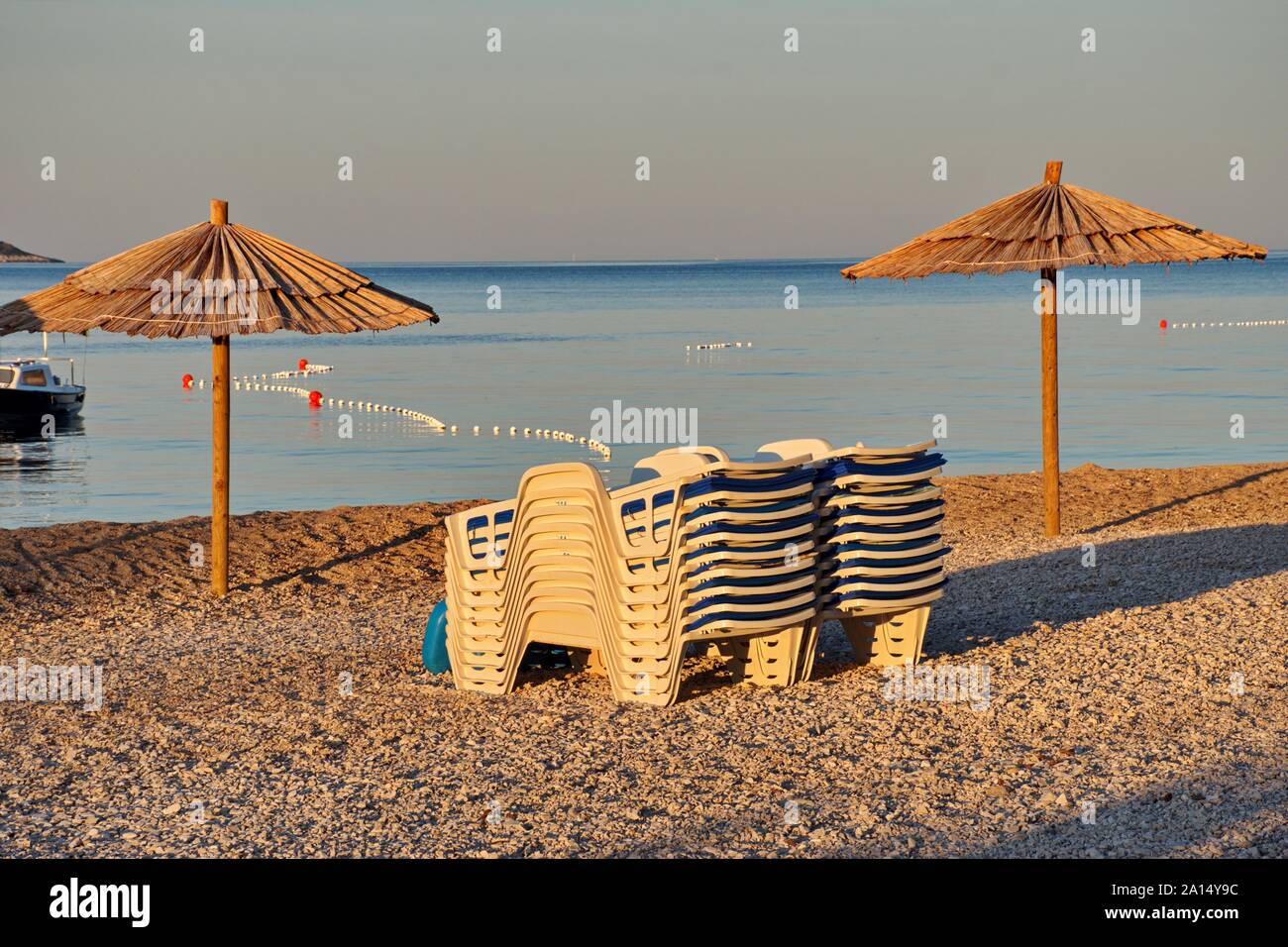 Sedie a sdraio e ombrelloni sulla spiaggia di ciottoli durante il sunrise Foto Stock