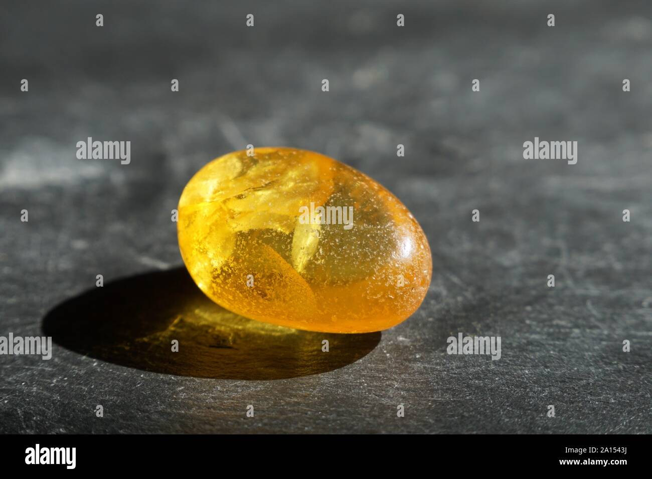 Giallo ambra pietra con inclusioni di forma lenticolare, su grigio ardesia, sfondo illuminato dal sole Foto Stock