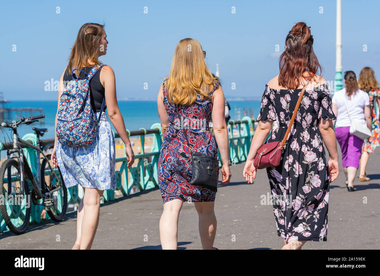 Femmine amici camminare lungo la passeggiata sul lungomare vestita per l'estate su un caldo estati soleggiate giorno in Brighton, East Sussex, Inghilterra, Regno Unito. Foto Stock