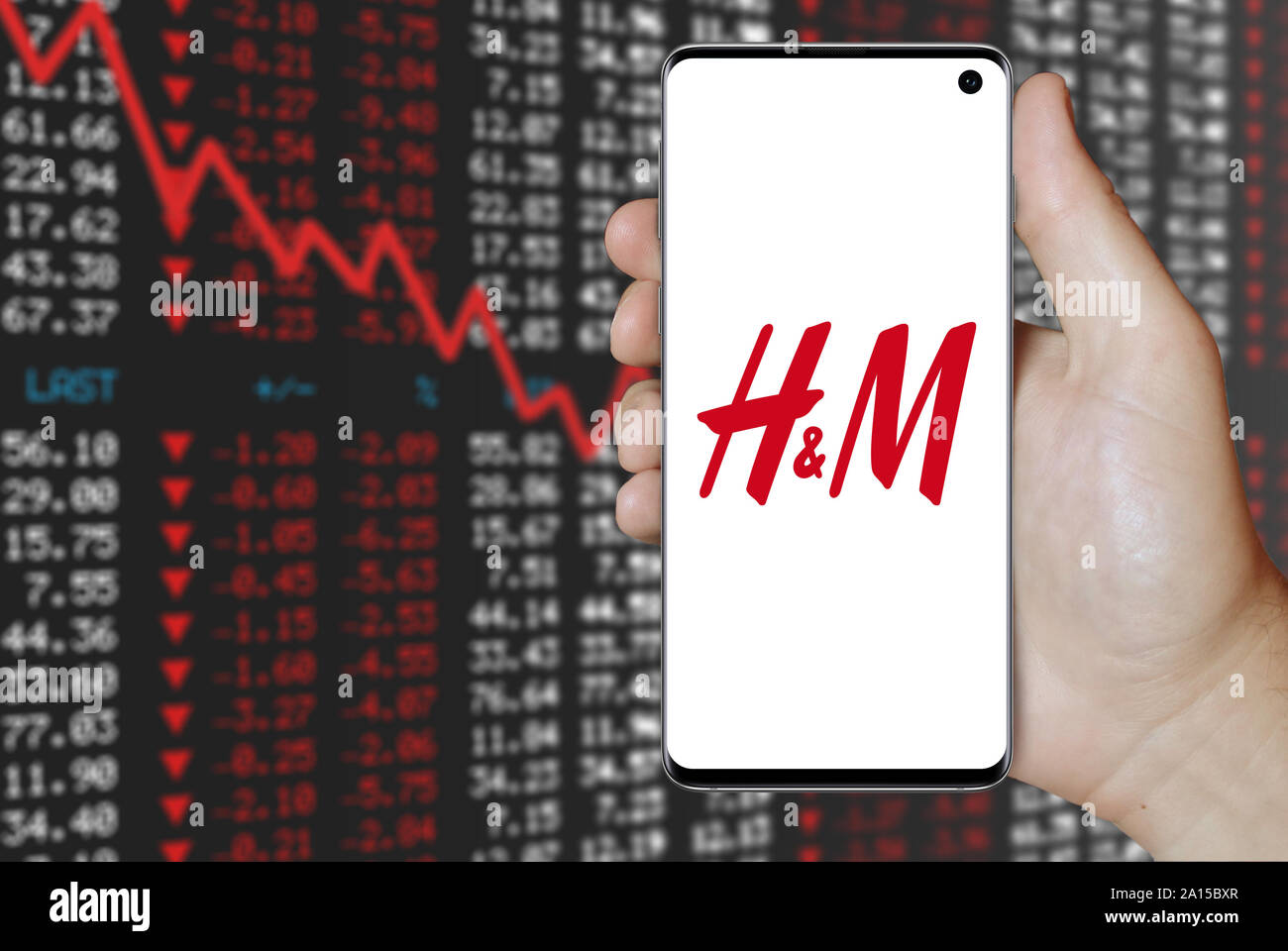 Un uomo possiede uno smartphone visualizzando il logo della società Hennes & Mauritz elencati su OMX di Stoccolma. Stock negativi sullo sfondo del mercato. Credito: PIXDUCE Foto Stock